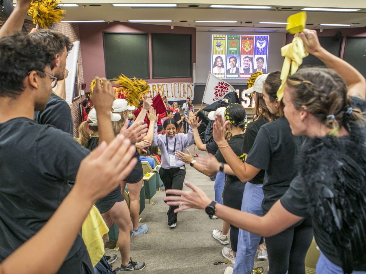 A female student, with arms raised, runs through a human tunnel of cheering VUSM students holding pom-poms.