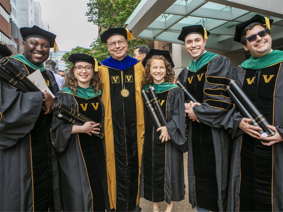 A smiling group of VUSM graduates in caps and gowns poses for a photo with Dean Jeffrey R. Balser.